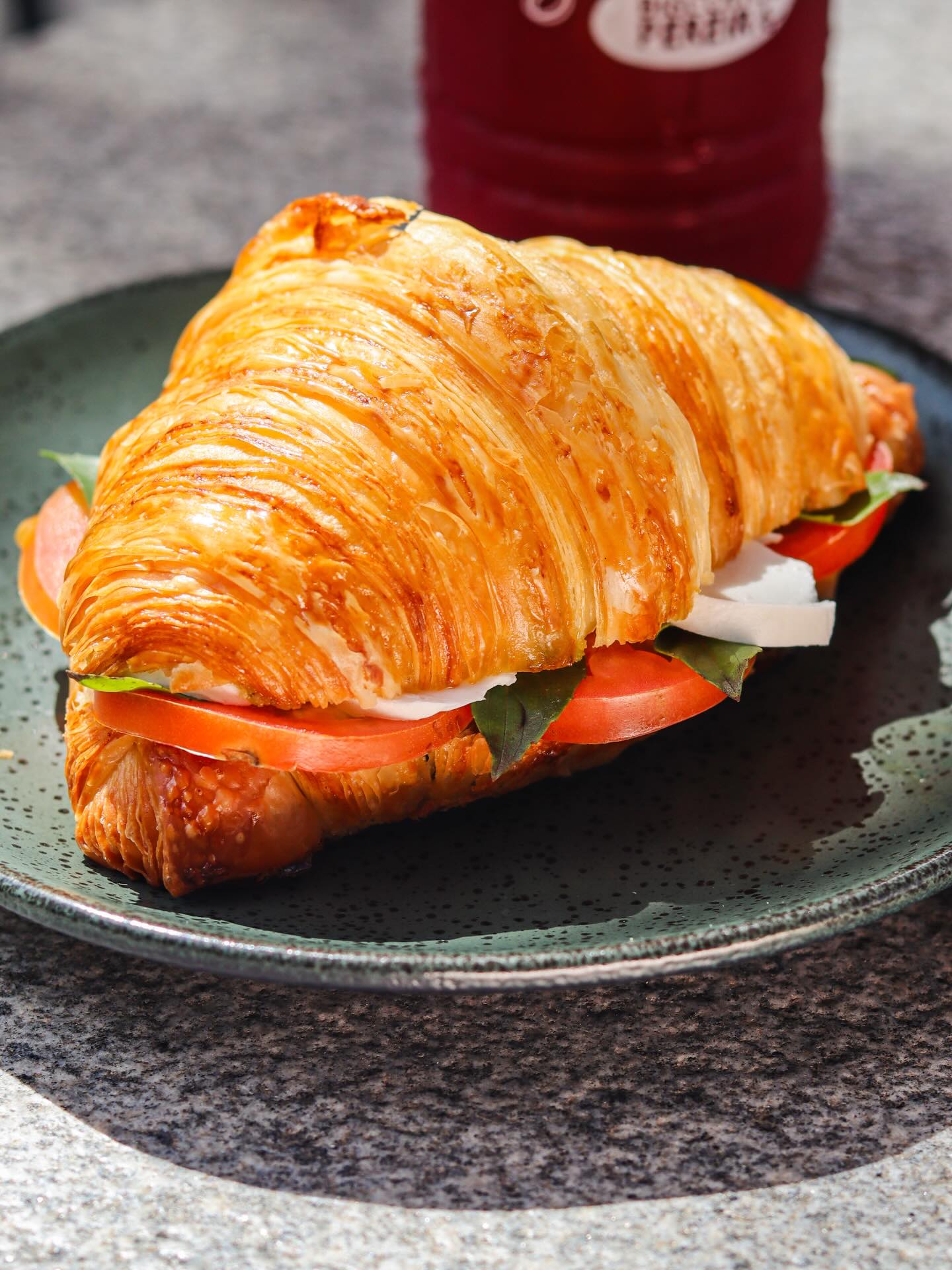 Croissant caprese com tomate, mussarela e manjericão em prato verde