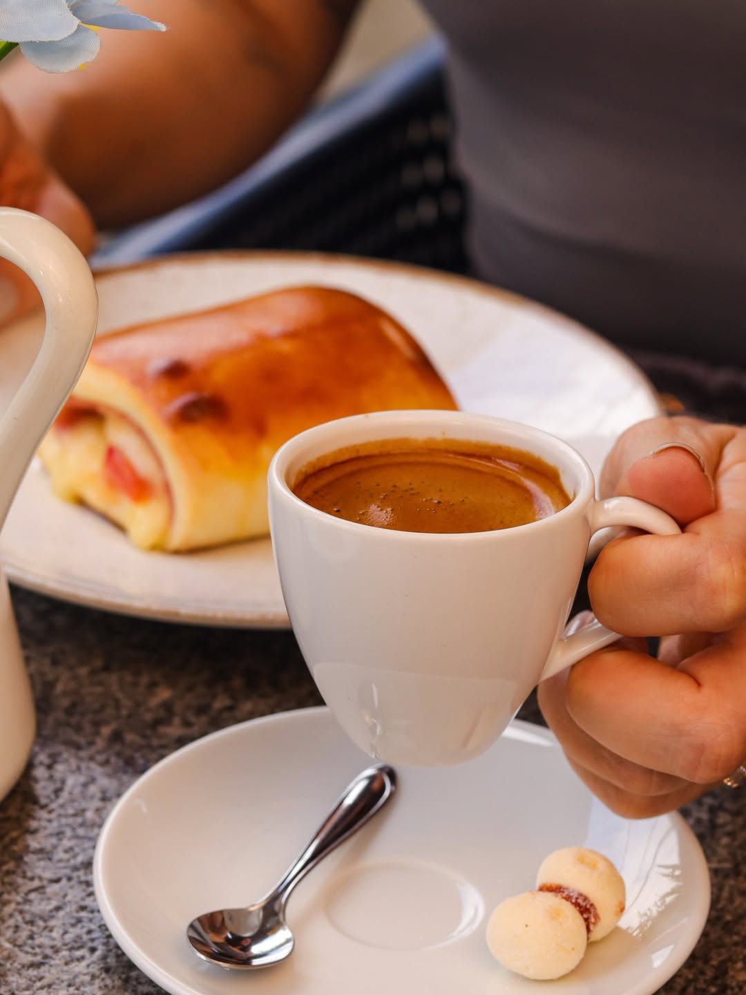 Xícara de café expresso com enroladinho de presunto e queijo ao fundo