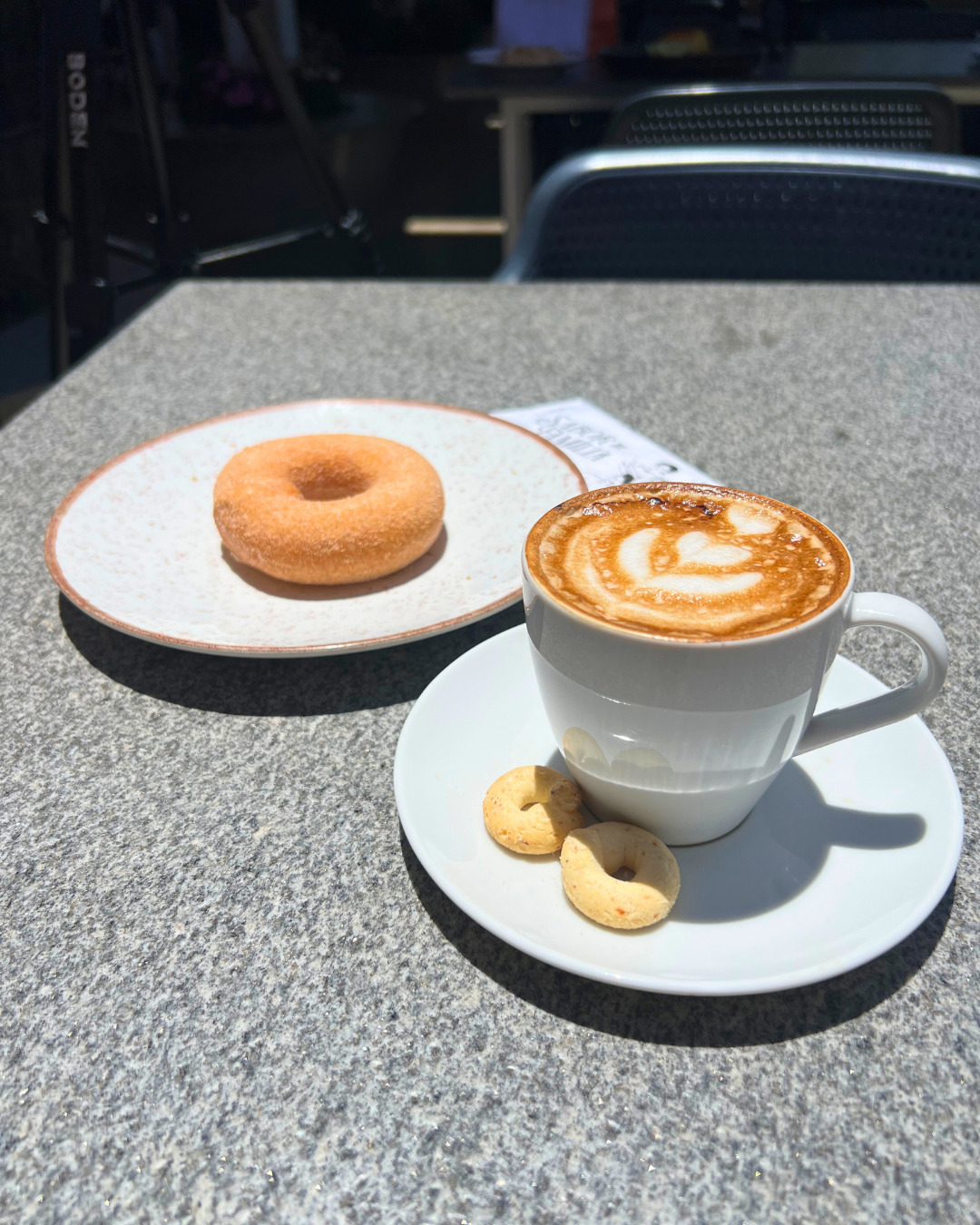 Xícara de café com latte art acompanhada de rosquinha e biscoitos de polvilho